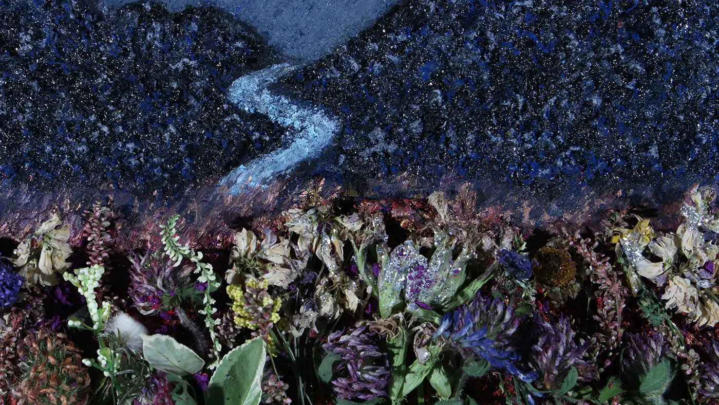 Floral installation with dried flowers in the foreground and a textured blue landscape backdrop featuring a winding river under a night-sky-like scene.