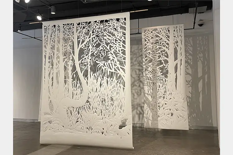 Two large tapestries of cut paper hanging from the ceiling showing woodland nature scenes Two large tapestries of cut paper hanging from the ceiling showing woodland nature scenes