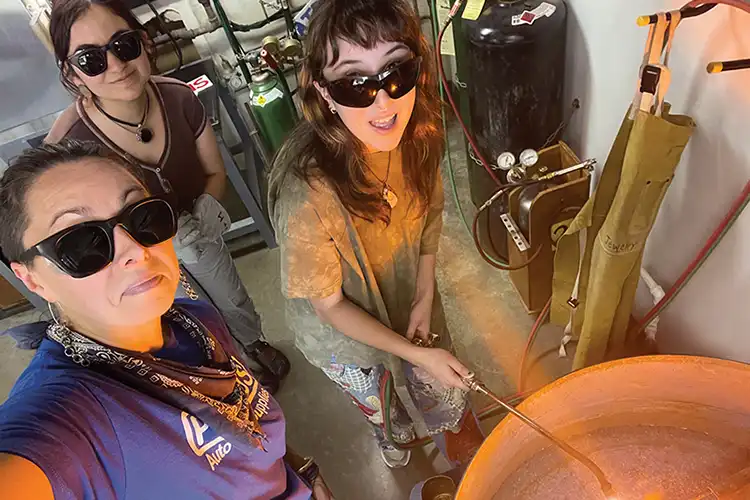 Meier poses with two students smiling over a foundry kiln.