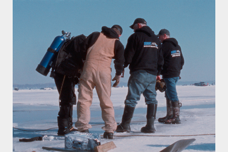 three men, one in diving gear, surrounding a hole in a sheet of ice three men, one in diving gear, surrounding a hole in a sheet of ice