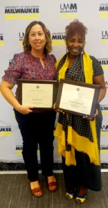 Two people stand holding award plaques.