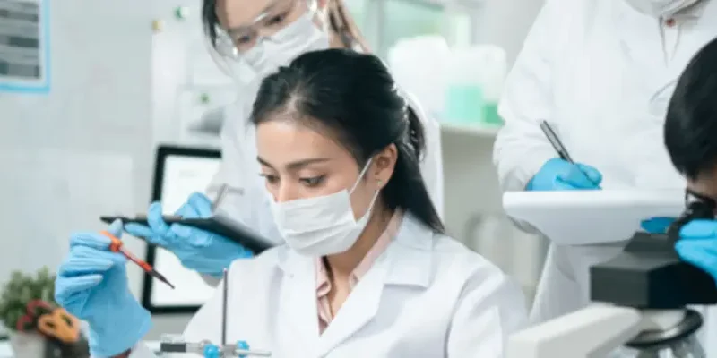 people working in a lab; focus on one masked person putting something into a test tube