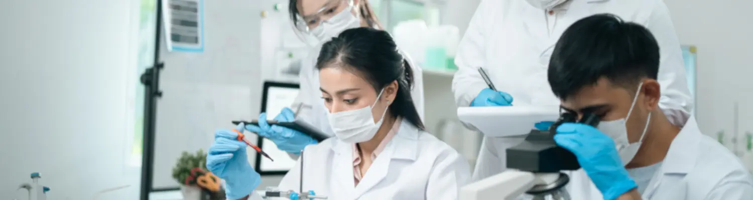 people working in a lab; focus on one masked person putting something into a test tube
