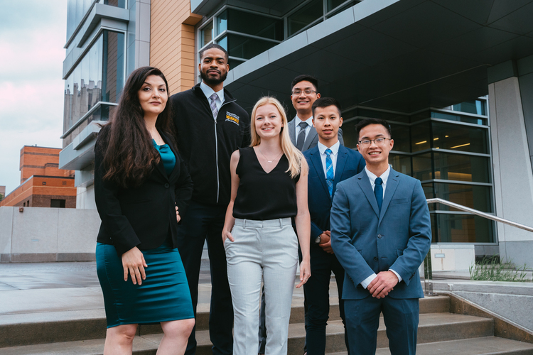 A group Health Care Administration students dresses in business attire (suits and ties and blazers) pose for a professional group shot before a conference.