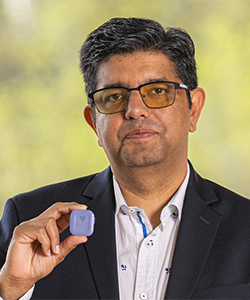 Man with dark hair and glasses holding a small tracking device in his hand