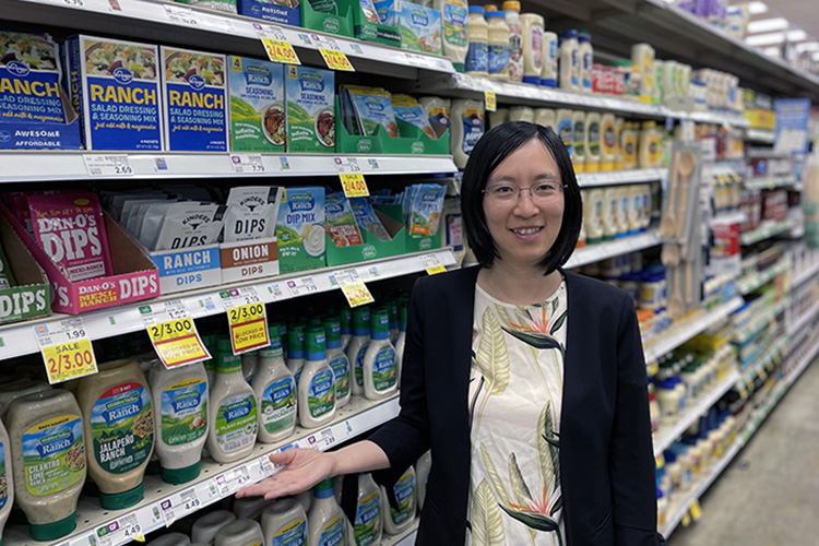 Woman with short dark hair and glasses standing in front of a grocery store shelf with bottles of ranch dressing with the same price