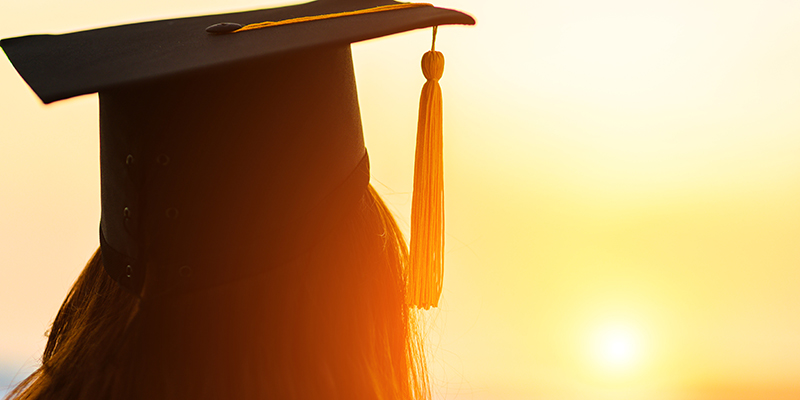 Silhouette of a person wearing a graduate cap with a gold background