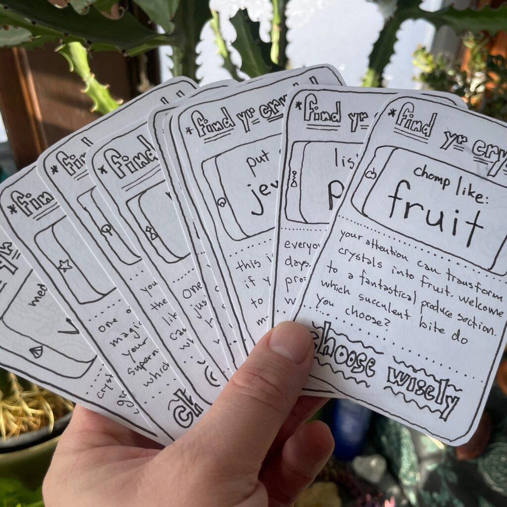 A hand holding a deck of cards with various prompts that read, "find your crystal."