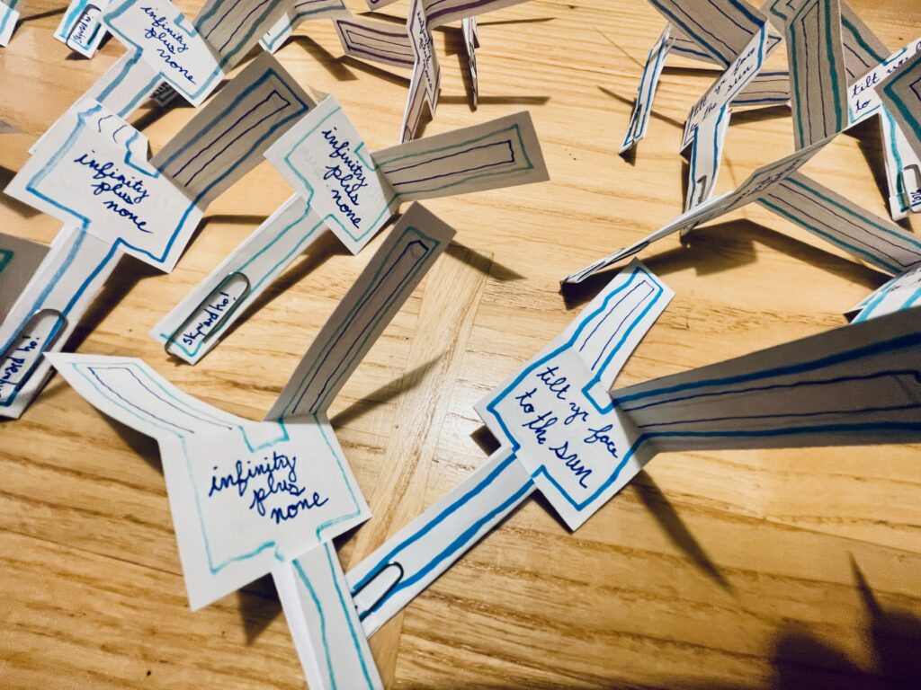 Several paper helicopters on a wooden table that read "Infinity plus none" and "Tile your face to the sun."