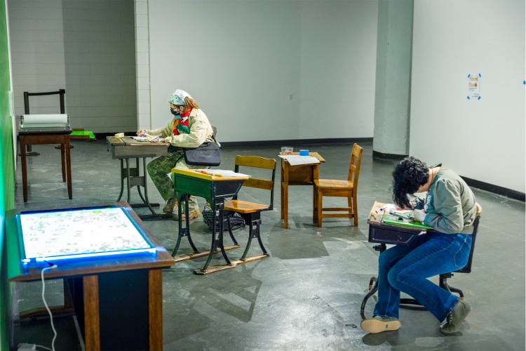 Installation shot of the Generation to Generation exhibition from C21's Aesthetics, Art, & AI program series, featuring two gallery guests seated at desks that ate part on an installation. Their heads are bowed over a work surface, suggesting deep engagement with an interactive artwork. Installation shot of the Generation to Generation exhibition from C21's Aesthetics, Art, & AI program series, featuring two gallery guests seated at desks that ate part on an installation. Their heads are bowed over a work surface, suggesting deep engagement with an interactive artwork.