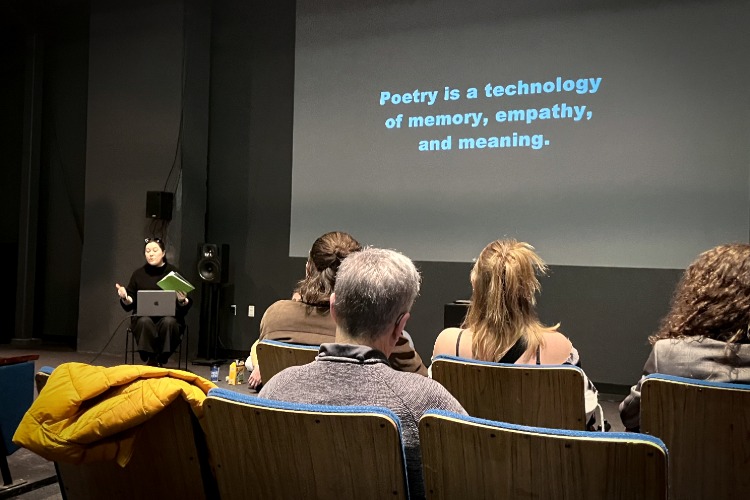 A slide projected onto a wall that says "Poetry is a technology of memory, empathy, and meaning," from the Language as Collaborator: Co-Creating with Thinking Machines workshop, part of C21's Aesthetics, Art, & AI program series.