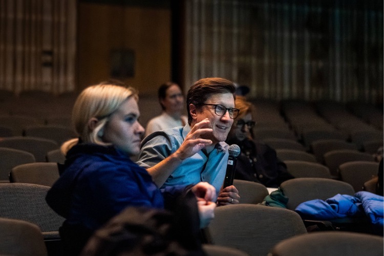 A graduate assistant holds a microphone for an audience member asking a question during Kite's artist talk, part of C21's Aesthetics, Art, & AI program series. A graduate assistant holds a microphone for an audience member asking a question during Kite's artist talk, part of C21's Aesthetics, Art, & AI program series.