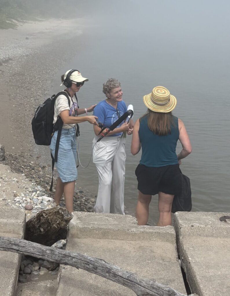 Melissa Scanlan, a reporter, and a sound tech in conversation at the beach