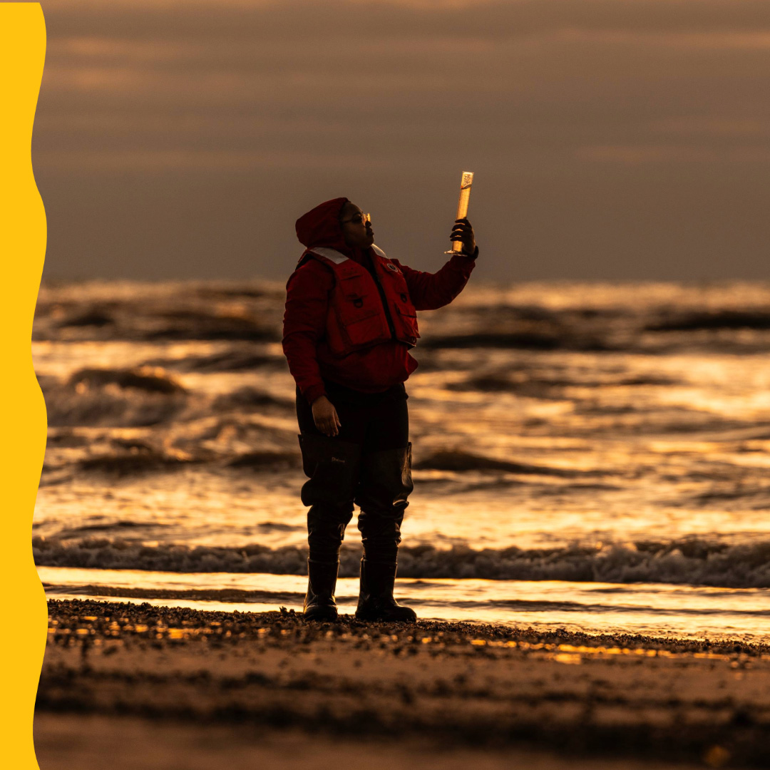 Person stands on beach and looks at test tube of lake water.