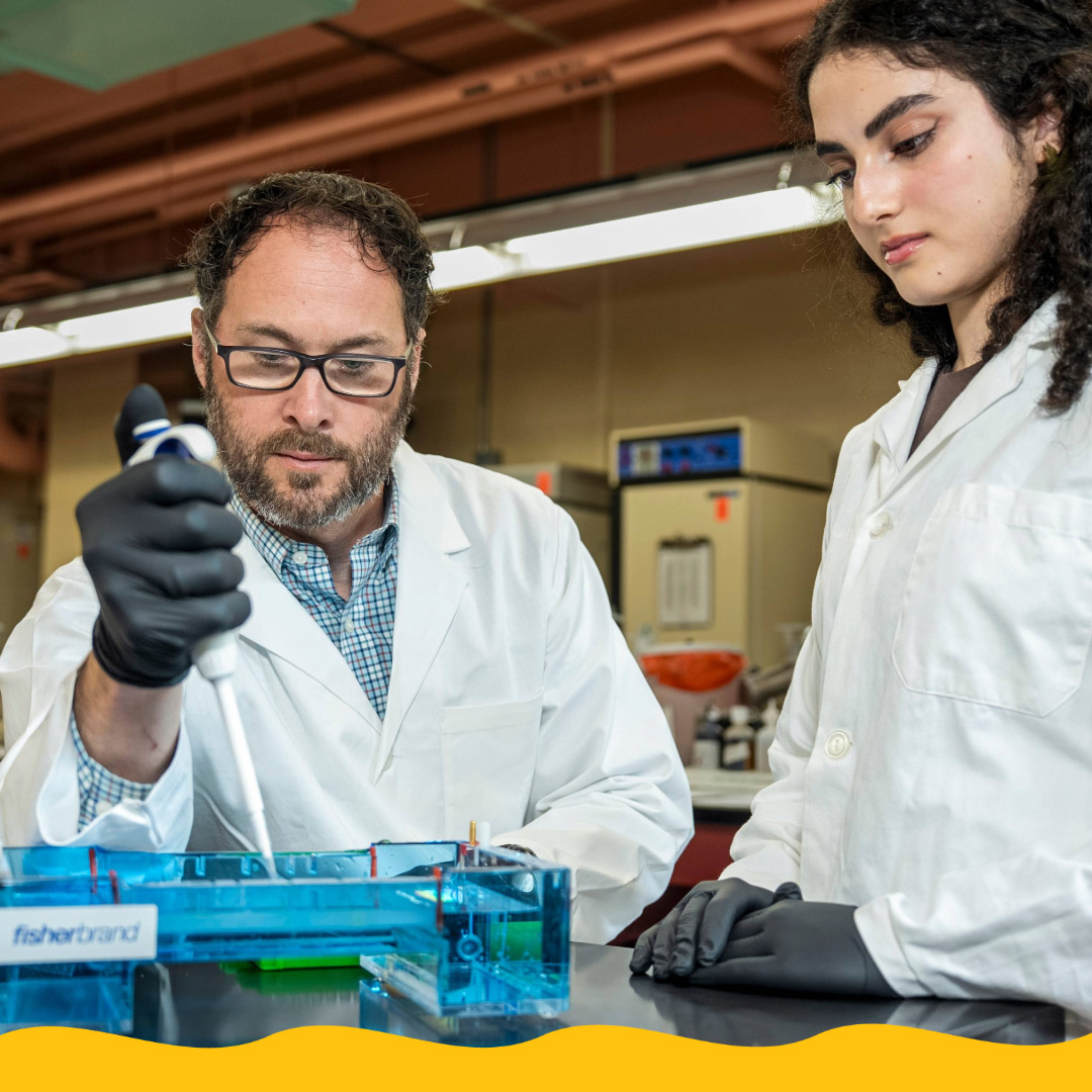 Two researchers wearing white coats work in lab.
