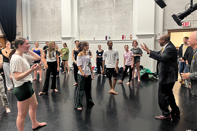 Chancellor Gibson stands with dozens of students who are in a dance class.