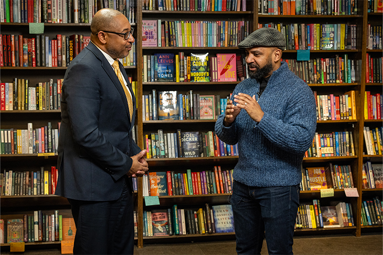 Chancellor Gibson talks with faculty member and poet Derrick Harriell, in a bookstore with books behind them.