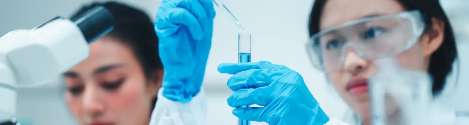 Two scientists in protective eyewear and gloves working with pipette and test tube filled with blue liquid in a lab