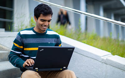 Male student in striped sweater smiling at laptop