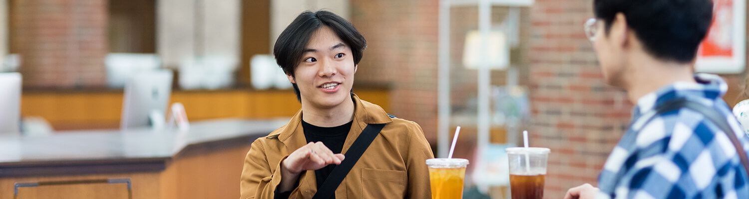 Male Asian student in tan shirt with an iced beverage in front of him