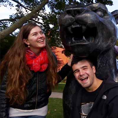 Smiling female white student in scarf, white male student smiling near Panther statue