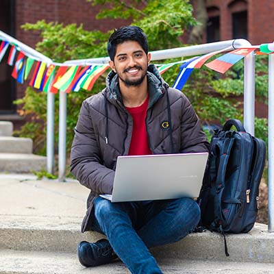 Indian student smiling at camera and working on his laptop