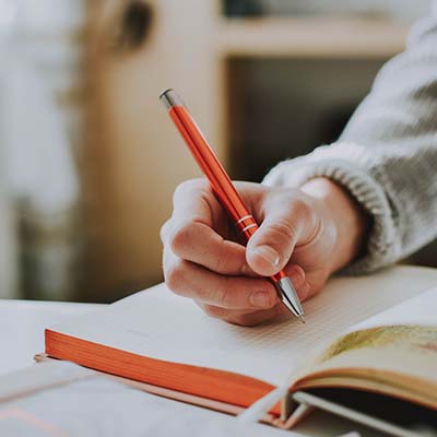 Person holding orange pen writing in a notebook