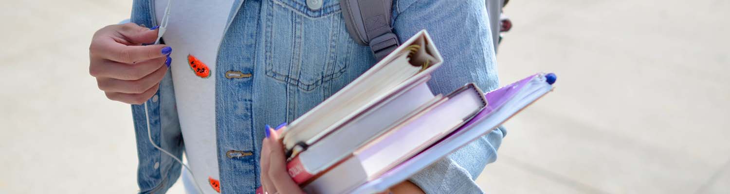 Student with jean jacket holding three textbooks