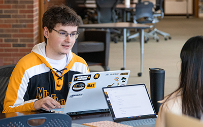 White male student in glasses looking across laptop
