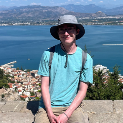 Male student on a bench overlooking a Grecian city and coastline
