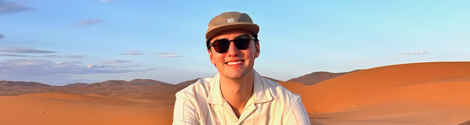 Male student smiling and sitting on sand dunes
