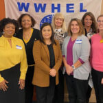 WWHEL members proudly standing together in front of a WWHEL banner.