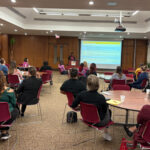 WWHEL members sitting in groups at circle tables while listening to someone speaking at the podium.