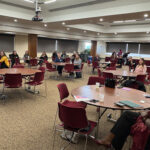 WWHEL members sitting in a conference room. The members are sitting at various circle tables and listening intently. 