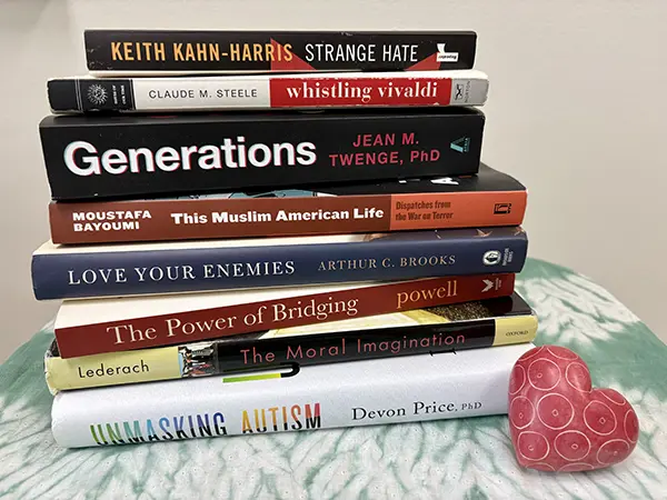 Stack of books showing spines and titles, with a heart-shaped paperweight beside the stack.