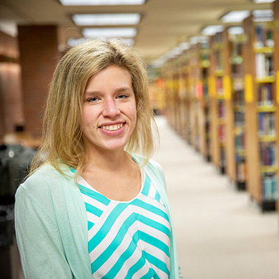 Dr. Abigail Phillips, Assistant Professor of Information Studiies standing in UWM Libraries near book stacks