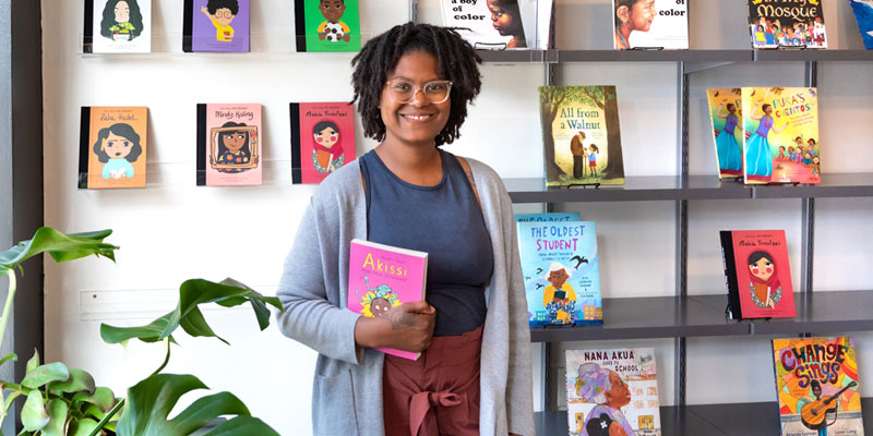Black woman holding books in her BIPOC bookstore.