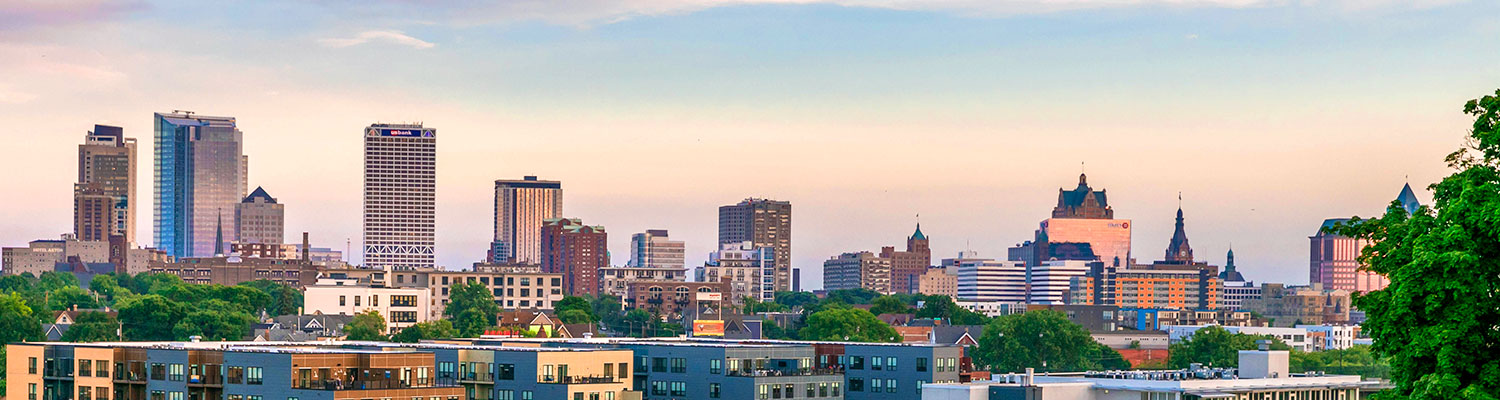 Skyline view of the city of Milwaukee against a pastel-colored sky.