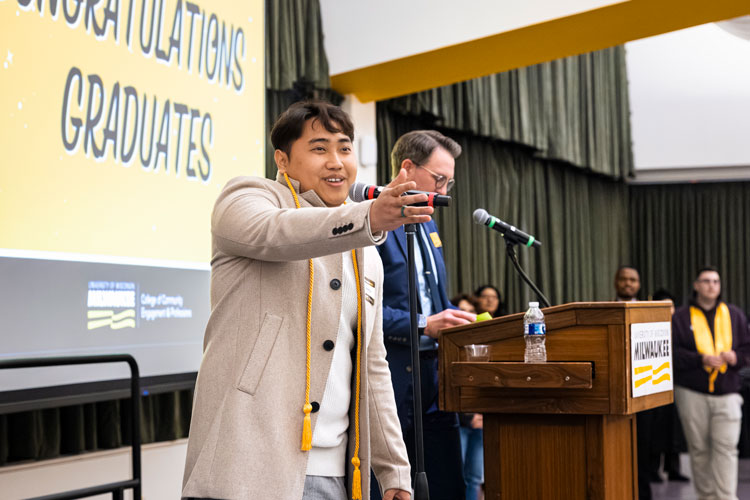 Male graduate on stage, standing at microphone, reaching out to audience