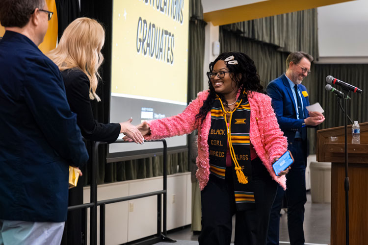 Female graduate on stage reaching out to shake hands with the Dean of the College of Community Engagement and Professions