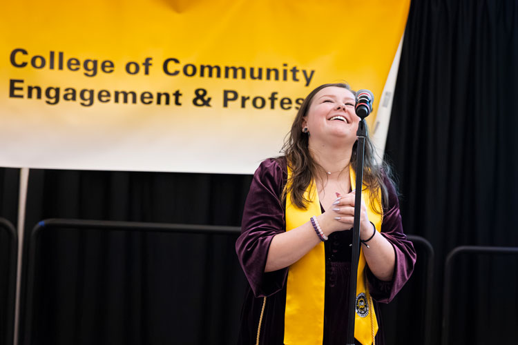 Female graduate with folded hands and large smile standing at microphone