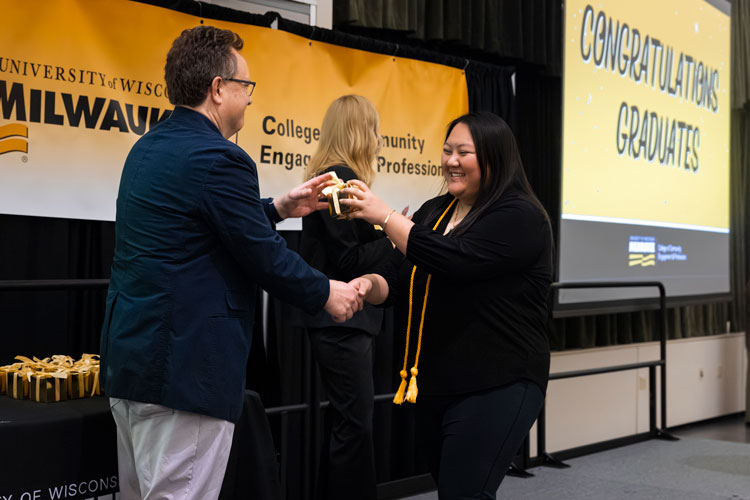 Smiling graduate shaking hands with faculty member on stage and accepts a small gift
