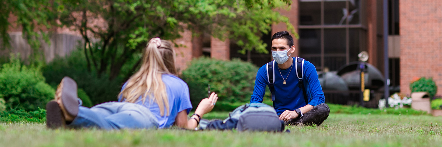 Students sitting in grass wearing masks