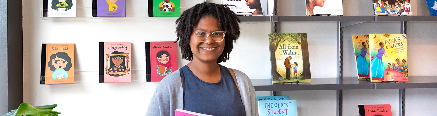 School of Education alumna Ashley Valentine (african american woman), poses for a picture inside of her bookstore and tutoring center named Rooted MKE