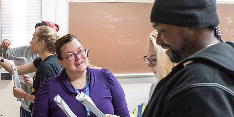 School of Education doctoral student Leah Rineck (white woman) engaging with students who are working through math equations on the classroom chalkboard