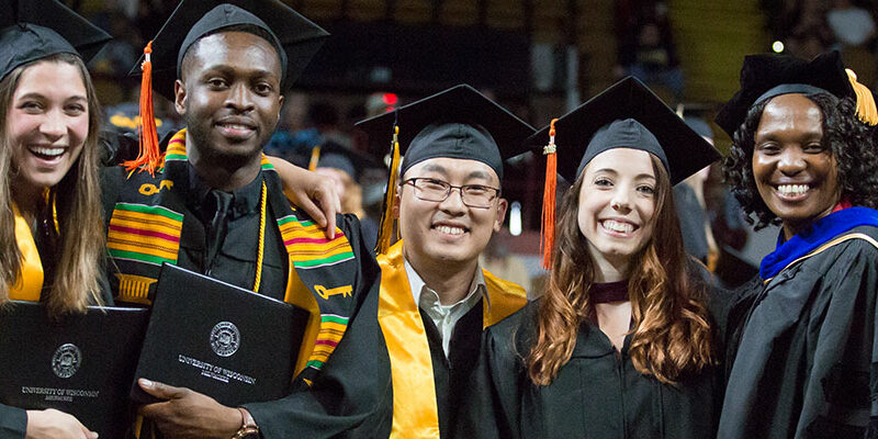A diverse group of UW-Milwaukee graduates posing for a picture with their diplomas at the graduation ceremony.