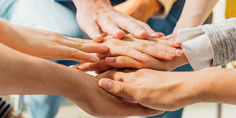 Individuals place their hands together in a sign of unity and teamwork