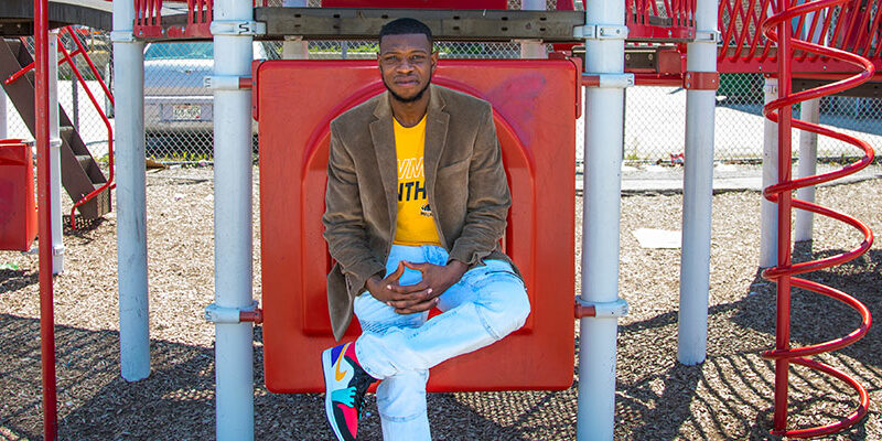 Student teacher (black man) sitting on some school playground equipment