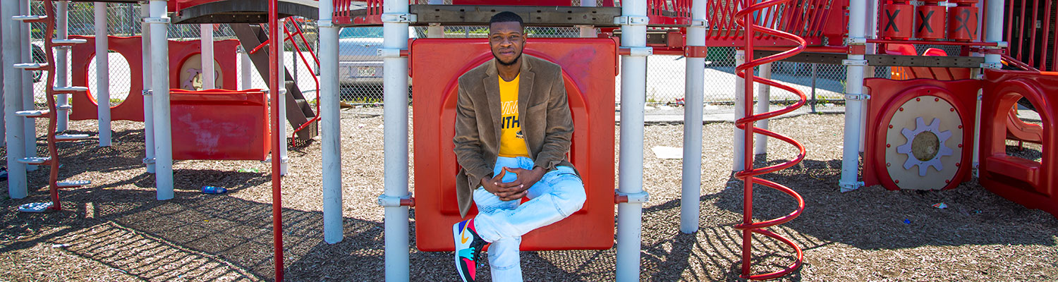 Student teacher (black man) sitting on some school playground equipment