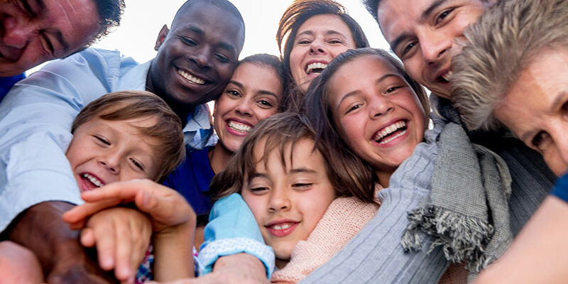 Adults and children huddle together and put their hands together in a pile while smiling and laughing.